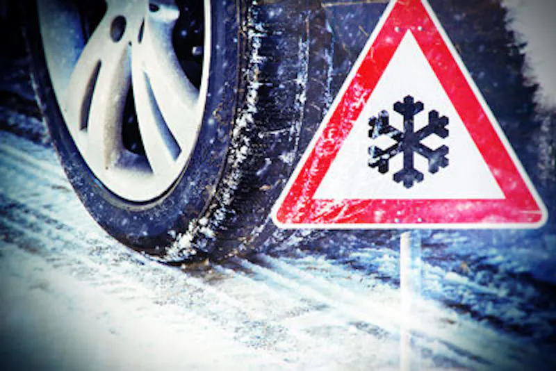 Vinterdäck på snötäckt väg med varningsskylt för halka